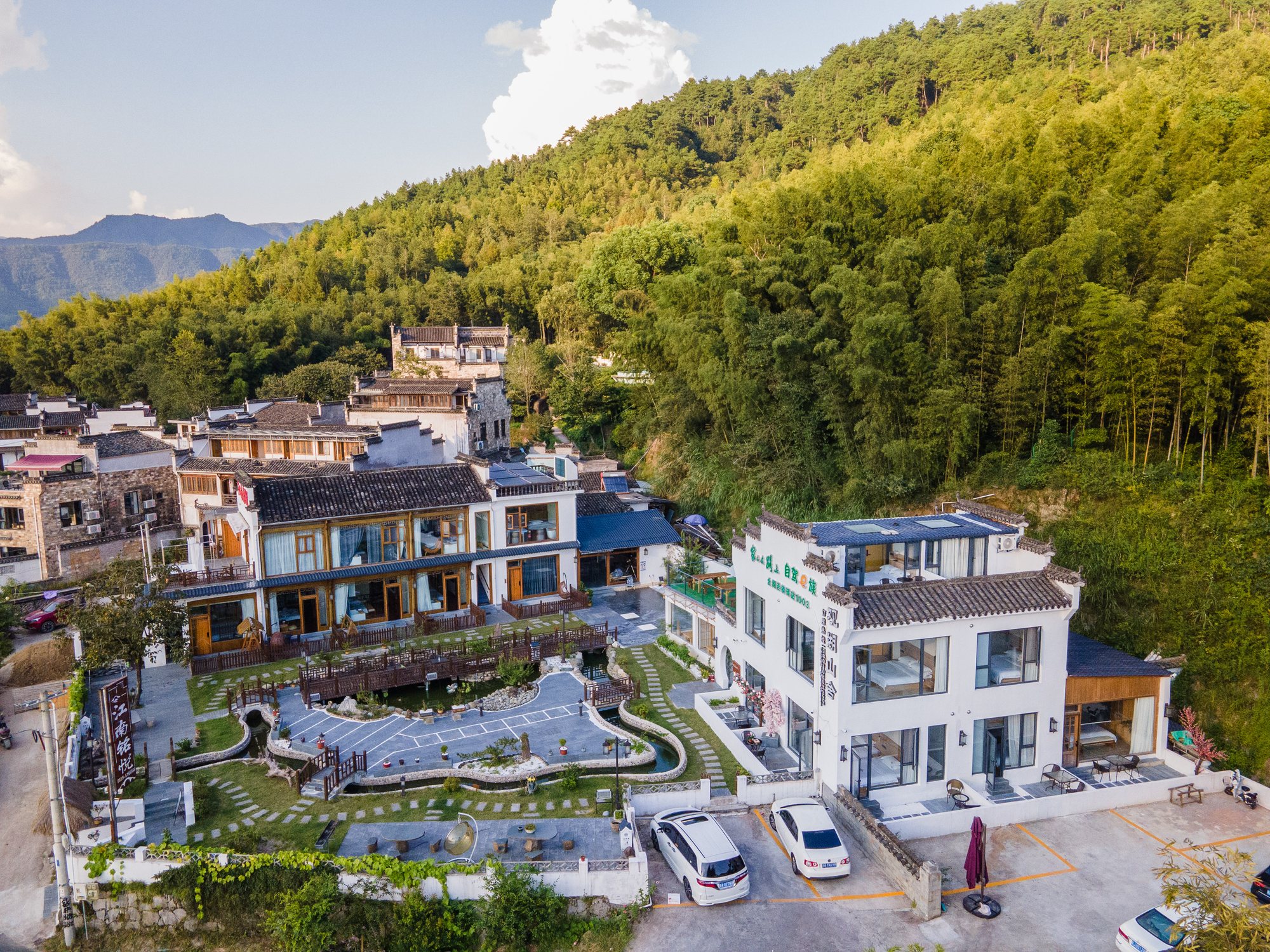 民宿外景航拍，白墙黛瓦嵌在山坳竹林之间